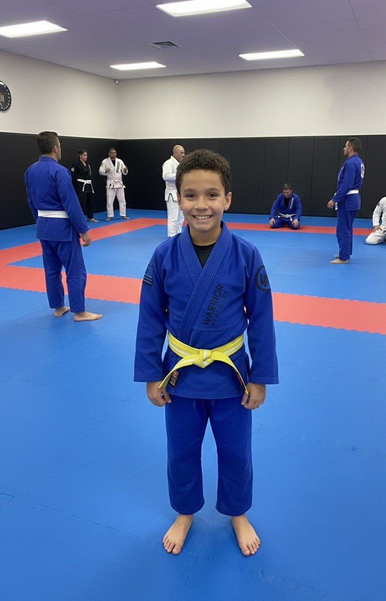 Child in blue martial arts uniform with yellow belt standing in a dojo.