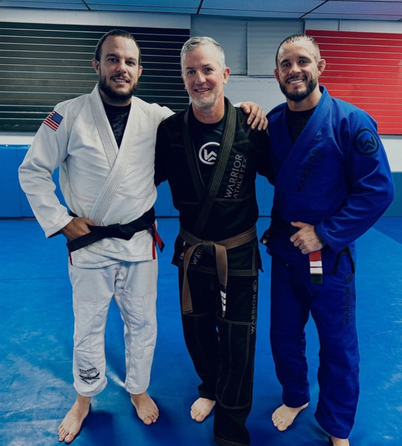 Three individuals in martial arts uniforms standing together on a blue mat.