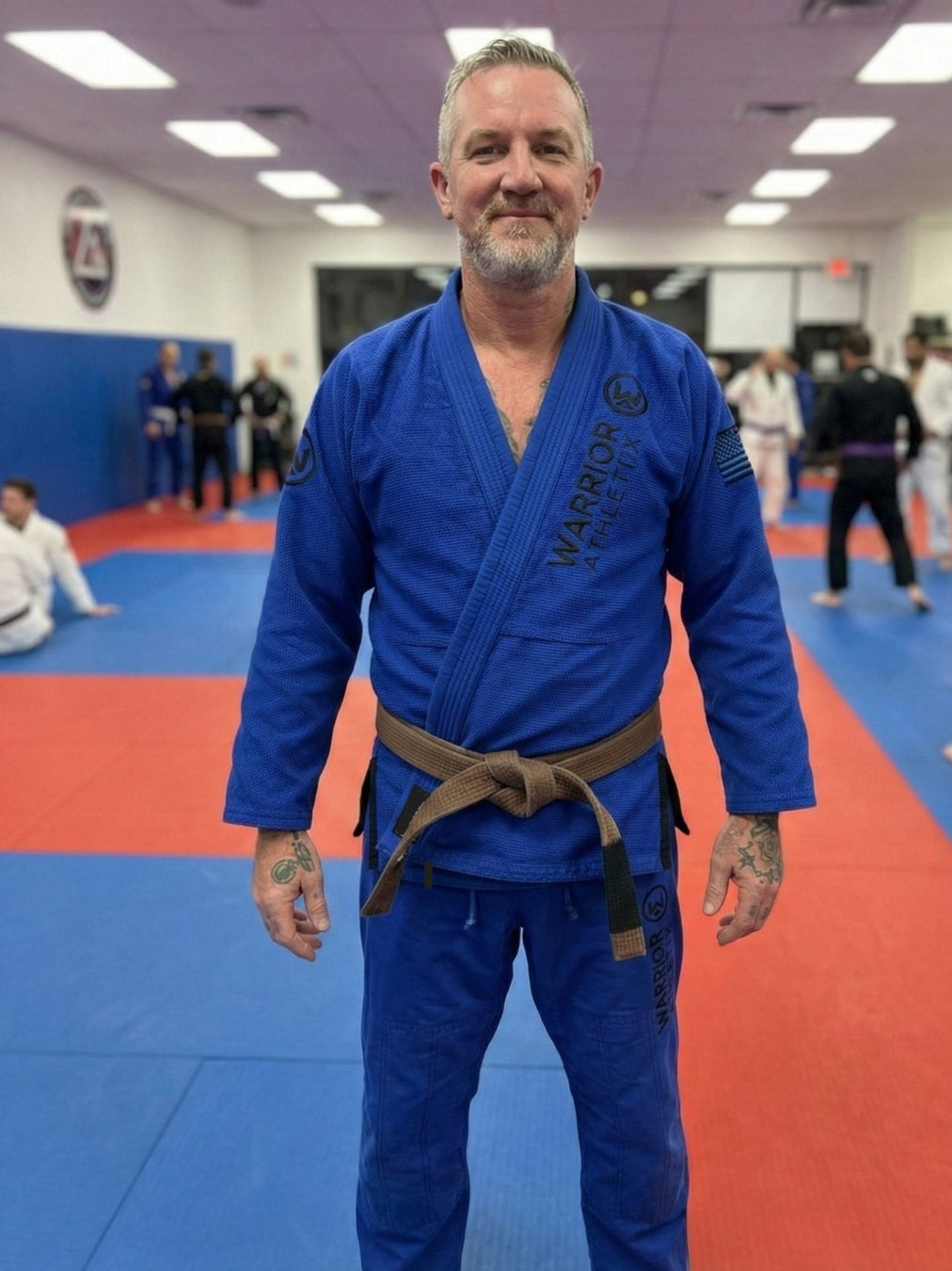 Man in a blue martial arts uniform standing on a red and blue mat.